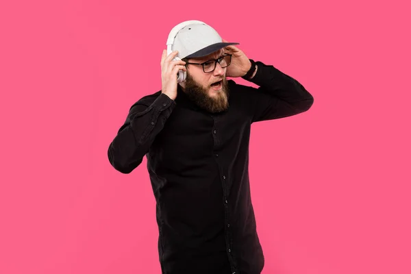 Disappointed bearded male hipster taking off headphones isolated on pink — Stock Photo