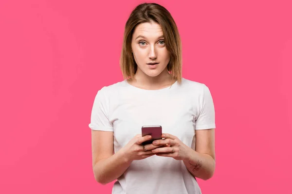 Giovane donna con smartphone guardando la fotocamera isolata su rosa — Foto stock