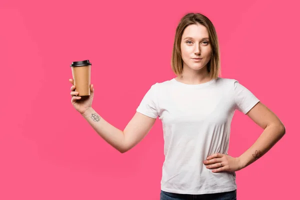 Alegre tatuado menina mostrando descartável xícara de café isolado no rosa — Fotografia de Stock