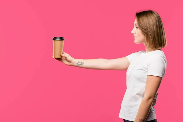 Vista lateral da menina mostrando copo descartável de café isolado em rosa — Fotografia de Stock