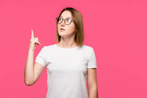 Mujer joven en gafas haciendo gesto de idea aislado en rosa - foto de stock