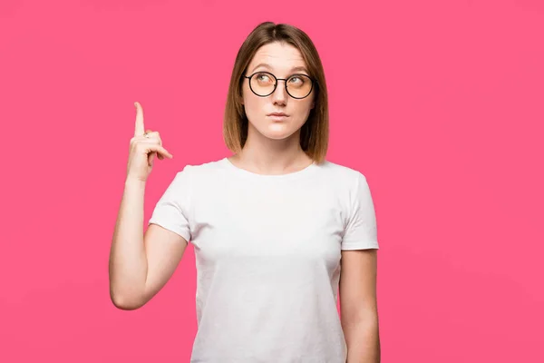 Attractive young woman in eyeglasses doing idea gesture isolated on pink — Stock Photo