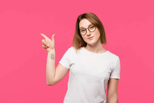 Happy stylish girl with tattooed hand pointing by finger isolated on pink — Stock Photo