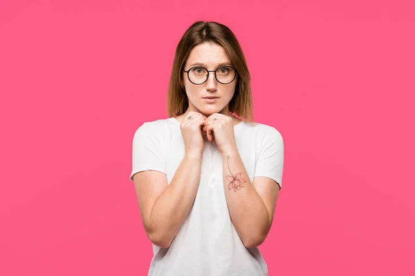 Verängstigtes tätowiertes Mädchen mit Brille blickt isoliert auf rosa Kamera — Stockfoto