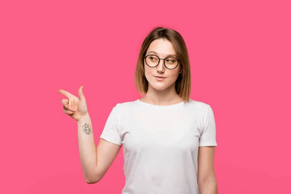 Stylish girl with tattooed hand pointing by finger isolated on pink — Stock Photo