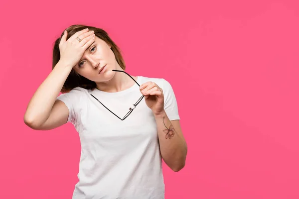 Young woman holding eyeglasses while having headache isolated on pink — Stock Photo