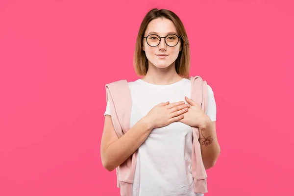 Menina elegante em óculos de mãos dadas no peito isolado em rosa — Fotografia de Stock