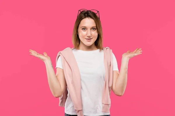 Mujer joven positiva haciendo gesto de encogimiento aislado en rosa - foto de stock