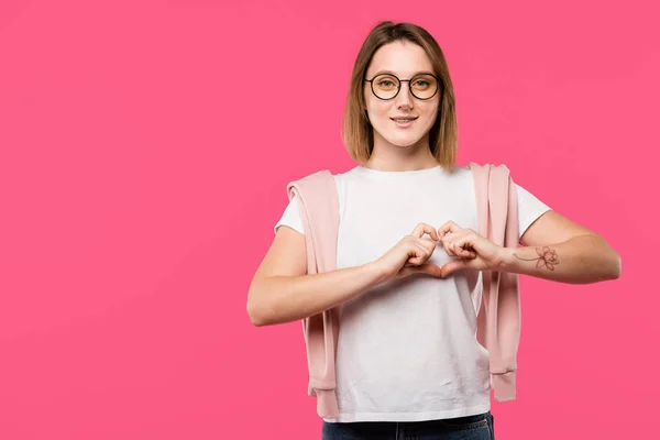 Fille gaie dans les lunettes montrant symbole de coeur isolé sur rose — Photo de stock