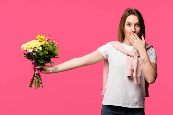 Молода жінка покриває рот вручну і дарує барвистий букет з різних квітів ізольовані на рожевому — стокове фото