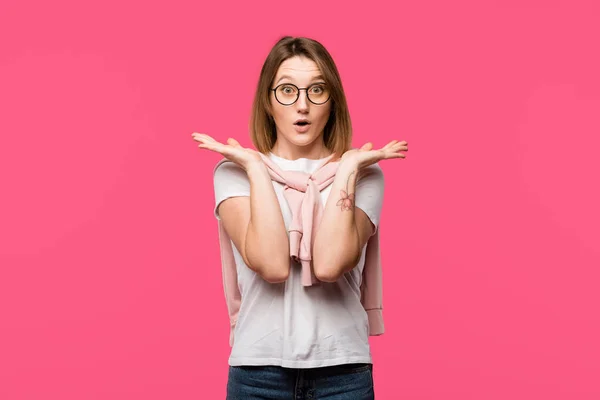 Шокована жінка в окулярах жестикулює руками ізольовано на рожевому — стокове фото
