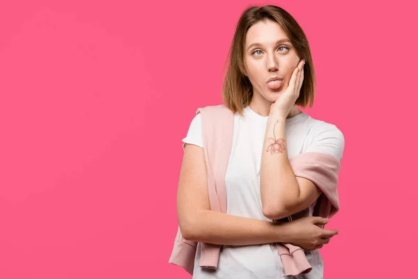 Junge Frau macht Fratze mit herausstreckender Zunge auf rosa — Stockfoto