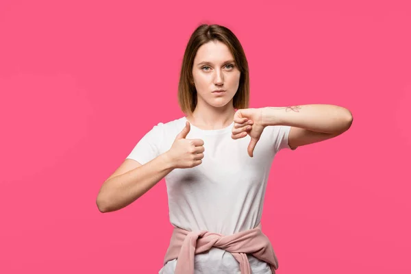 Jovem mulher mostrando polegar para cima e polegar para baixo isolado em rosa — Fotografia de Stock