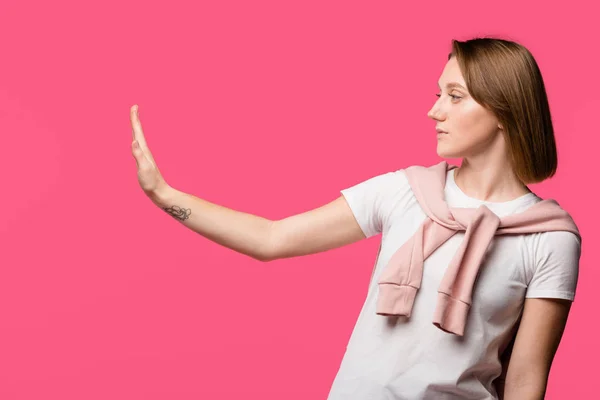 Vista lateral de la mujer joven mostrando gesto de stop aislado en rosa - foto de stock