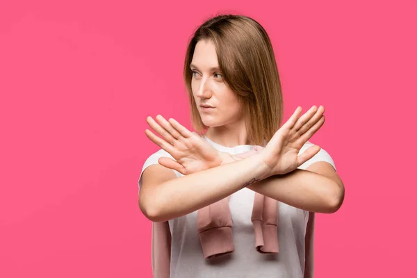 Mujer joven mirando hacia otro lado y mostrando gesto de stop con brazos cruzados aislados en rosa - foto de stock