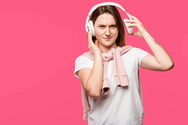 Irritated young woman taking off headphones isolated on pink — Stock Photo
