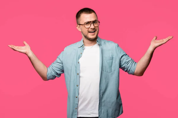 Hombre guapo en gafas de pie con los brazos abiertos y sonriendo a la cámara aislado en rosa - foto de stock
