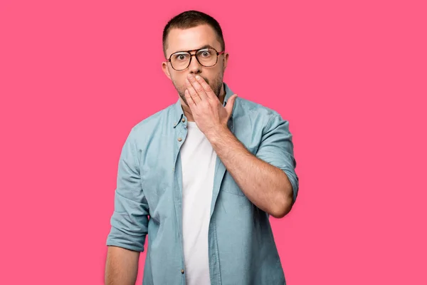 Schockierter junger Mann hält Hand über den Mund und blickt isoliert in die Kamera auf rosa — Stockfoto
