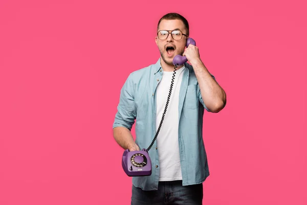 Shocked man in eyeglasses talking by vintage telephone and looking at camera isolated on pink — Stock Photo