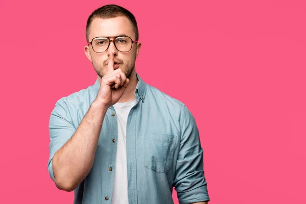 Young man gesturing for silence with finger on lips and looking at camera isolated on pink — Stock Photo