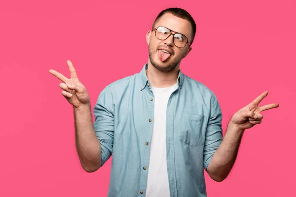 Divertido joven en gafas que muestran la lengua aislado en rosa - foto de stock