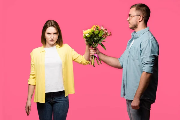 Young man presenting bouquet of flowers to angry woman isolated on pink — Stock Photo