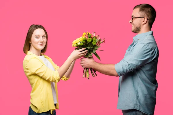 Jovem feliz apresentando buquê de flores a mulher sorridente isolado em rosa — Fotografia de Stock