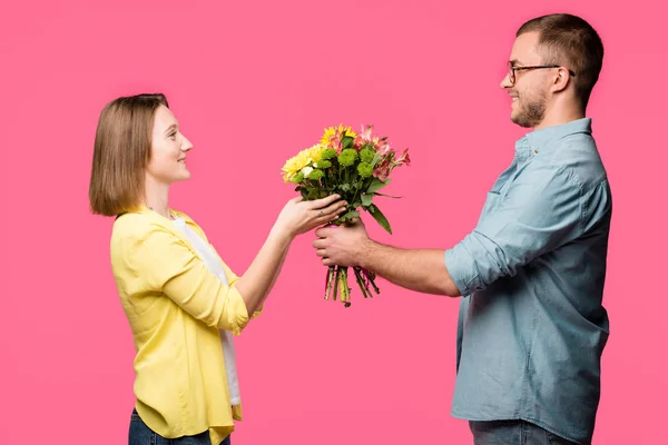 Vue latérale du jeune couple heureux tenant bouquet de fleurs isolé sur rose — Photo de stock