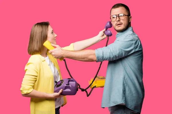 Seitenansicht eines jungen Paares, das Telefone und Hörer füreinander hält, isoliert auf rosa — Stockfoto