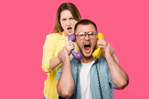 Jeune femme tenant des combinés et homme en lunettes criant isolé sur rose — Photo de stock