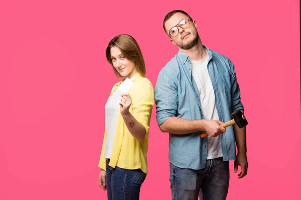 Young couple with hammer and blank card looking at camera isolated on pink — Stock Photo