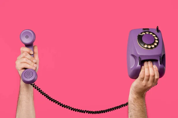 Обрізаний знімок людини, що тримає фіолетовий роторний телефон ізольований на рожевому — стокове фото