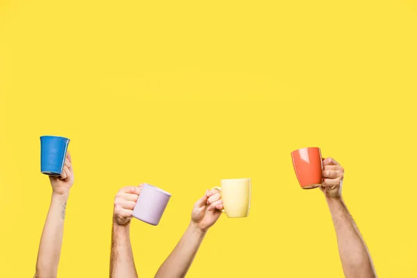 Cropped shot of male and female hands holding colorful cups isolated on yellow — Stock Photo