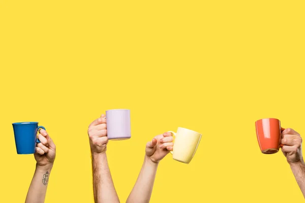 Partial view of people holding colorful cups isolated on yellow — Stock Photo