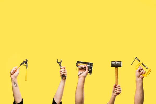 Обрезанный снимок рук, держащих степлер, гаечный ключ, ручной клапан, молоток, изолированный на желтом — стоковое фото