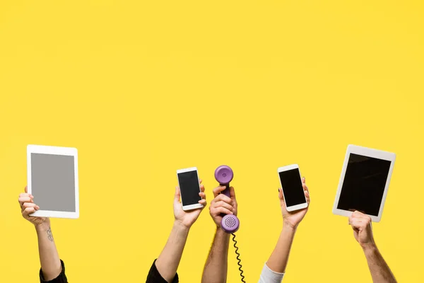 Recortado tiro de manos sosteniendo teléfonos inteligentes, tabletas digitales y auriculares aislados en amarillo - foto de stock