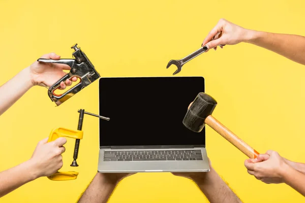 Recortado tiro de manos sosteniendo herramientas y portátil con pantalla en blanco aislado en amarillo - foto de stock