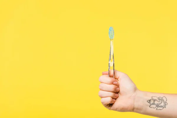 Tiro recortado de la persona que sostiene el cepillo de dientes aislado en amarillo - foto de stock