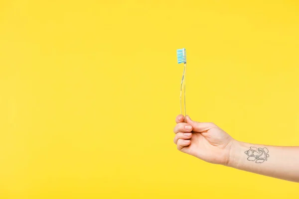 Tiro recortado de la persona que sostiene el cepillo de dientes aislado en amarillo - foto de stock