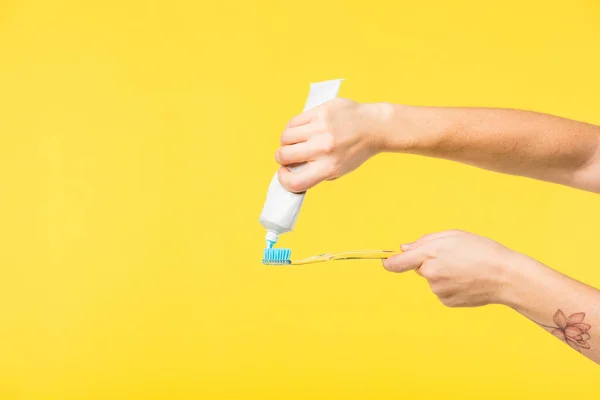 Colpo ritagliato di persona che tiene lo spazzolino da denti e dentifricio isolato su giallo — Foto stock