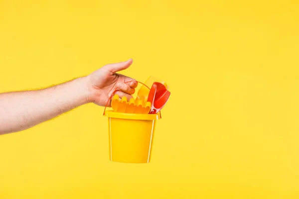 Tiro recortado de la persona sosteniendo cubo de plástico con juguetes aislados en amarillo - foto de stock