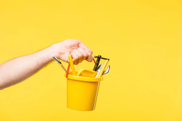 Tiro recortado de la persona sosteniendo cubo de plástico con juguetes y herramientas aisladas en amarillo - foto de stock