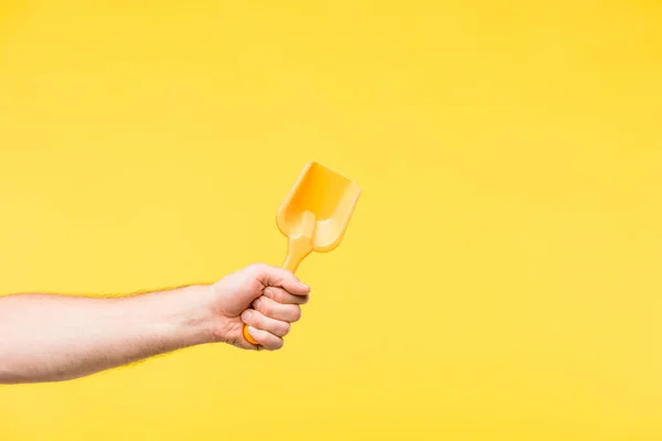 Cropped shot of person holding toy shovel isolated on yellow — Stock Photo