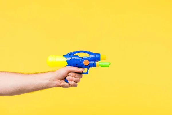 Tiro recortado de la persona sosteniendo pistola de juguete aislado en amarillo - foto de stock