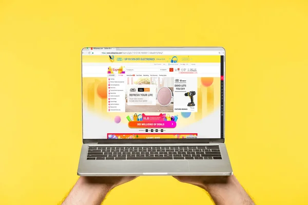 Cropped shot of person holding laptop with aliexpress website on screen isolated on yellow — Stock Photo