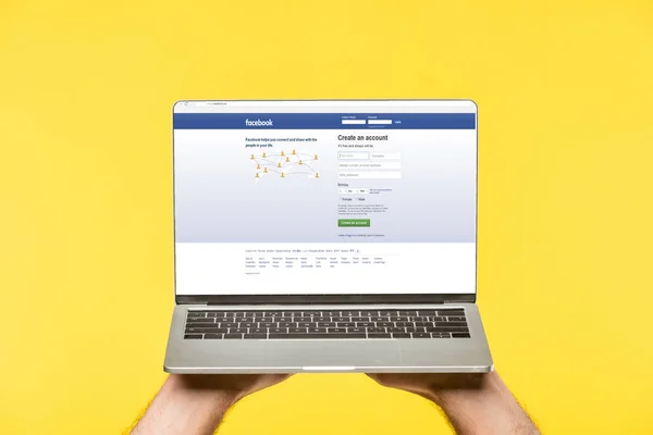 Tiro recortado de pessoa segurando laptop com site facebook na tela isolada no amarelo — Fotografia de Stock