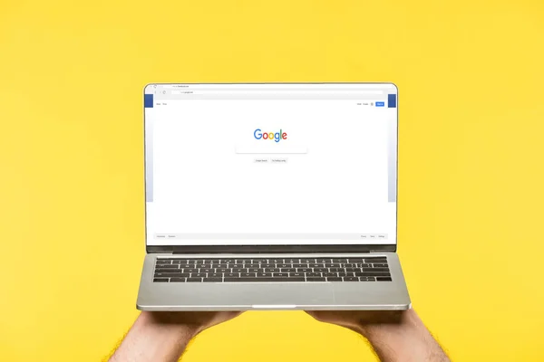 Recortado disparo de la persona que sostiene el ordenador portátil con el sitio web de Google en la pantalla aislada en amarillo - foto de stock