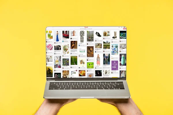 Colpo ritagliato di persona che tiene il computer portatile con il sito web pinterest sullo schermo isolato sul giallo — Foto stock