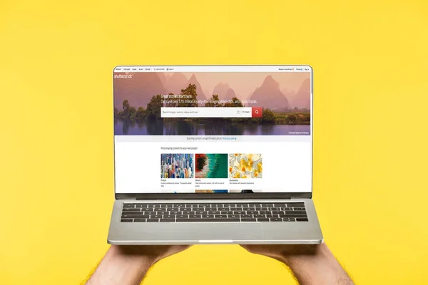 Cropped shot of person holding laptop with shutterstock website on screen isolated on yellow — Stock Photo