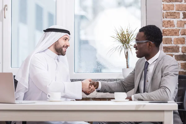 Empresarios multiculturales estrechando la mano en la oficina moderna - foto de stock